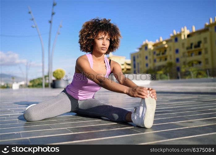Young black woman doing stretching after running outdoors. Girl exercising with city scape at the background. Afro hair.