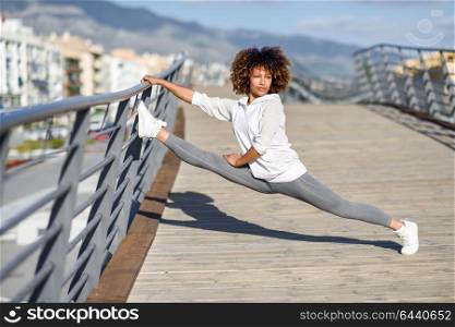Young black woman doing stretching after running outdoors. Girl exercising with city scape at the background. Afro hair.