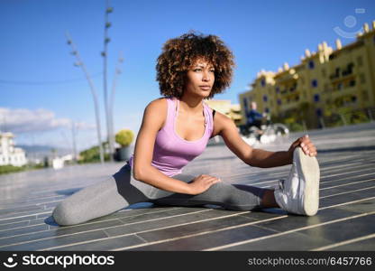 Young black woman doing stretching after running outdoors. Girl exercising with city scape at the background. Afro hair.