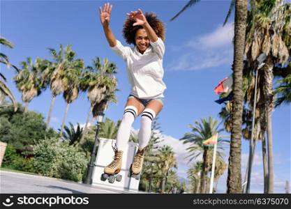 Young black woman on roller skates jumping near the beach. Girl with afro hairstyle rollerblading on sunny promenade.