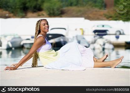 Young black woman sitting on the dock of a seaport wearing a nice summer dress.. Black woman sitting on the dock of a seaport wearing a nice summer dress.