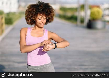 Young black woman using smartwatch touching touchscreen in active sports activity. Girl with afro hair looking at her smart watch screen.