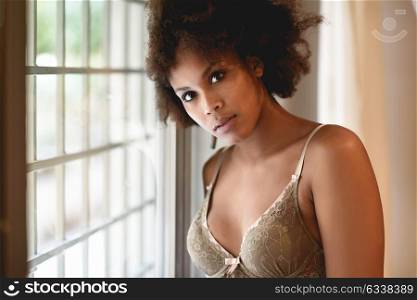 Young black woman with afro hairstyle in lingerie near a window. Mixed girl wearing underwear in her room.