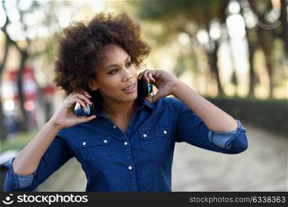 Young black woman with afro hairstyle listening to the music with headphones in urban background. Mixed funny woman wearing blue shirt and shorts.