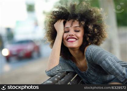 Young black woman with afro hairstyle smiling in urban background. Mixed girl wearing casual clothes.