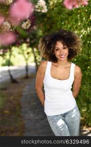 Young black woman with afro hairstyle smiling in urban park. Mixed girl wearing white t-shirt and blue jeans.