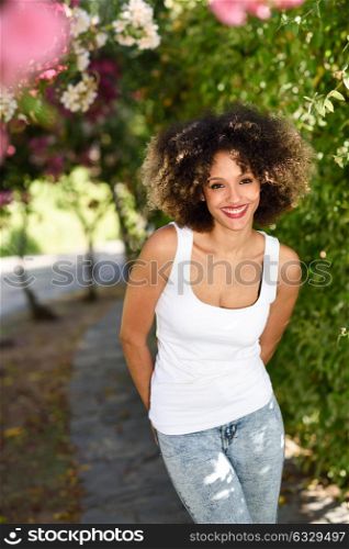 Young black woman with afro hairstyle smiling in urban park. Mixed girl wearing casual clothes.
