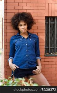 Young black woman with afro hairstyle standing in urban background. Mixed woman wearing blue shirt and shorts.