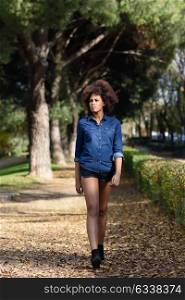 Young black woman with afro hairstyle walking in urban park. Mixed woman wearing blue shirt and shorts.