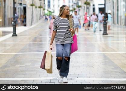 Young black woman, with coloured braids, with shopping bags in the street.. Black woman, with coloured braids, with shopping bags in the street.