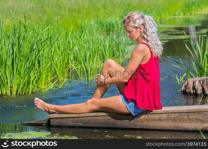 Young blond caucasian woman musing at water in nature