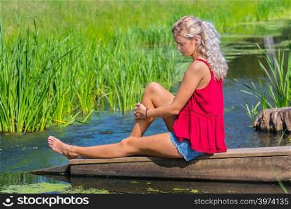 Young blond caucasian woman musing at water in nature