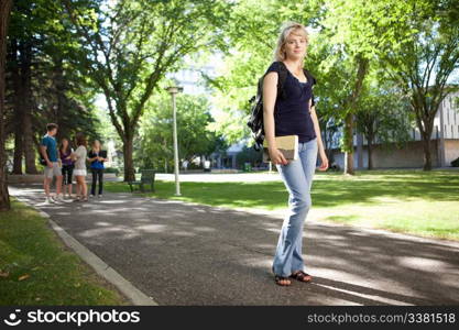 Young blond college girl walking to class with friends in background