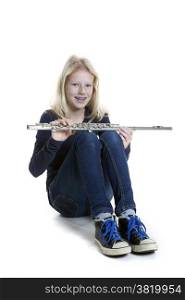 young blond girl sits holding flute in studio against white background