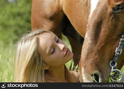 young blond teenager and her brown stallion in a field