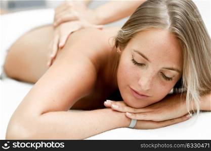 Young blond woman having massage in the spa salon. Massage and body care. Body massage treatment.