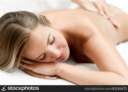 Young blond woman having massage in the spa salon. Massage and body care. Body massage treatment.