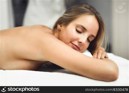 Young blond woman having massage in the spa salon. Massage and body care. Body massage treatment. Smiling female.