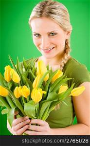 Young blond woman hold yellow tulips flower on green
