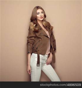 Young blond woman in brown jacket and white jeans. Girl posing on a beige background. Jewelry and hairstyle. Fashion photo
