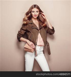 Young blond woman in brown jacket and white jeans. Girl posing on a beige background. Jewelry and hairstyle. Girl with brown handbag. Fashion photo