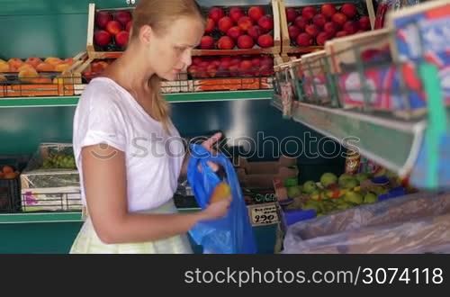 Young blond woman in fruit shop. While choosing pears she looking at them and smelling