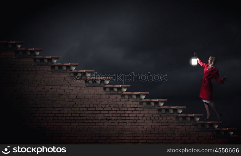 Young blond woman in red cloak with lantern lost in darkness. Woman with lantern