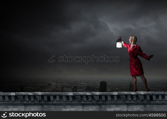 Young blond woman in red cloak with lantern lost in darkness. Woman with lantern