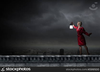 Young blond woman in red cloak with lantern lost in darkness. Woman with lantern