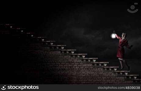 Young blond woman in red cloak with lantern lost in darkness. Woman with lantern