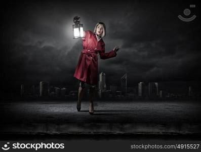 Young blond woman in red cloak with lantern lost in darkness. Woman with lantern