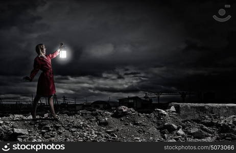 Young blond woman in red cloak with lantern lost in darkness. Woman with lantern