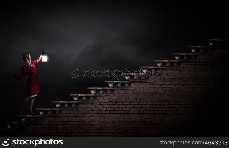 Young blond woman in red cloak with lantern walking in night. Lost in darkness