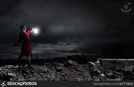 Young blond woman in red cloak with lantern walking in night. Lost in darkness