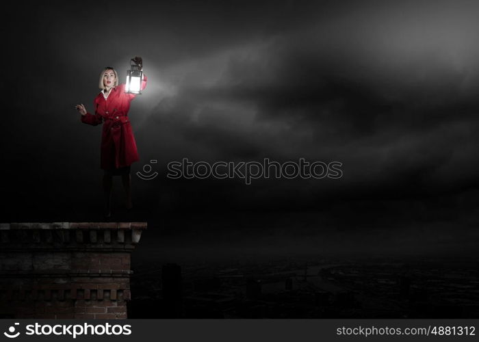 Young blond woman in red cloak with lantern walking in night. Lost in darkness