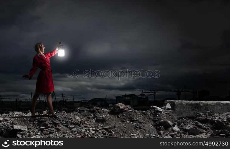 Young blond woman in red cloak with lantern walking in night. Lost in darkness