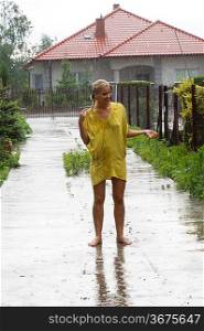 young blond woman in yellow dress under rain falling down outside of home