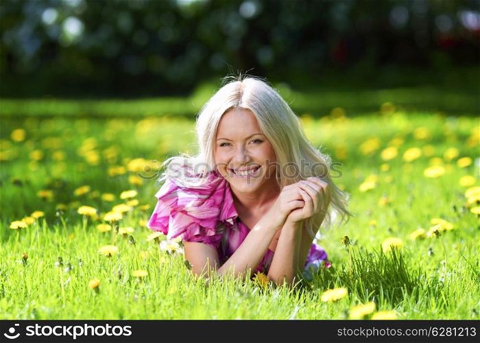 Young blond woman laying in a meadow with dandelions