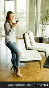 Young blond woman looking at cell phone while standing next in room