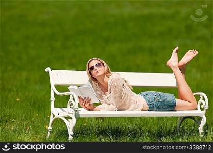 Young blond woman lying on white bench on sunny day; shallow DOF