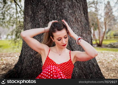 Young blond woman making a pigtail with red long dress