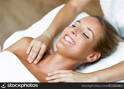 Young blond woman receiving a head massage in a spa center with eyes closed and smiling. Female patient is receiving treatment by professional therapist.