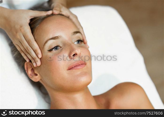 Young blond woman receiving a head massage in a spa center with blue eyes. Female patient is receiving treatment by professional therapist.. Young woman receiving a head massage in a spa center.