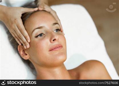 Young blond woman receiving a head massage in a spa center with blue eyes. Female patient is receiving treatment by professional therapist.. Young woman receiving a head massage in a spa center.