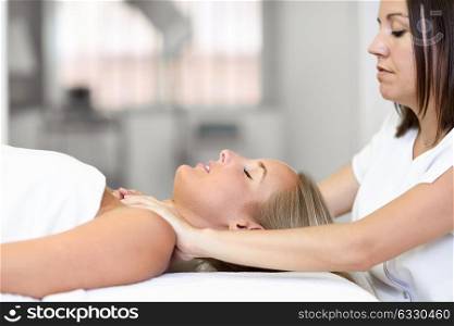 Young blond woman receiving a head massage in a spa center with eyes closed. Female patient is receiving treatment by professional therapist.