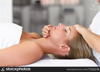 Young blond woman receiving a head massage in a spa center with eyes closed. Female patient is receiving treatment by professional therapist.. Young woman receiving a head massage in a spa center.