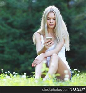 young blond woman sitting on grass. young blond woman with mobile phone sitting on grass