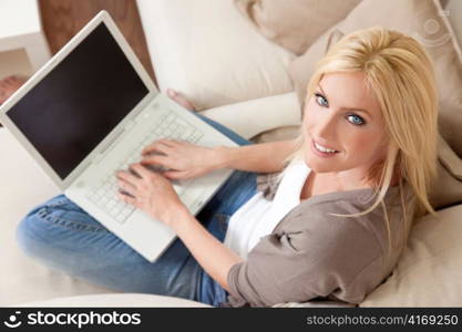 Young Blond Woman Using Laptop Computer At Home on Sofa