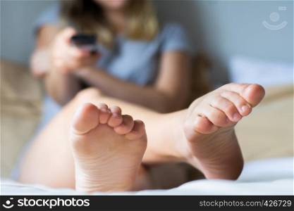 Young blond woman with remote lying in bed and watching tv. Television concept.