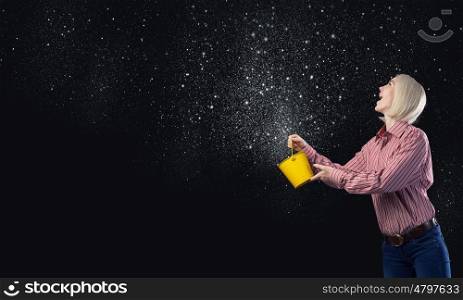 Young blond woman with yellow bucket in hands. Woman splashing stars from bucket